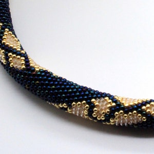 May include: A close-up of a beaded necklace featuring a dark blue and gold pattern. The necklace is crafted from small, round beads woven together in an intricate design.