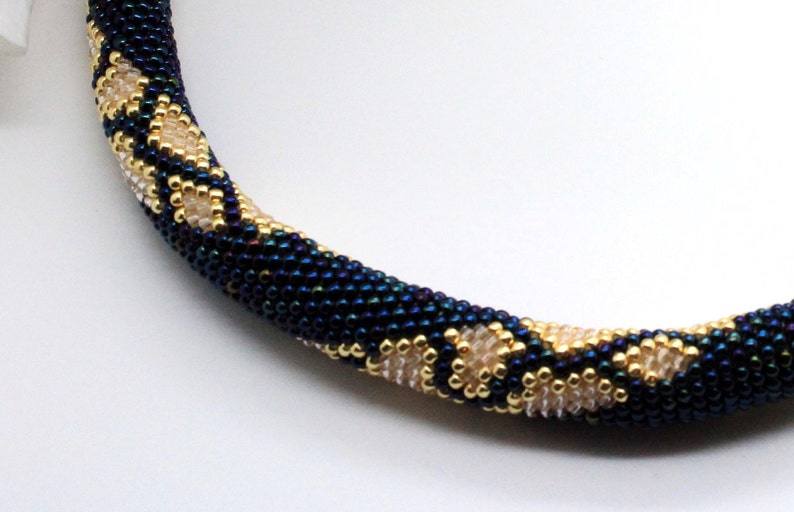 May include: A close-up of a beaded necklace featuring a dark blue and gold pattern. The necklace is crafted from small, round beads woven together in an intricate design.
