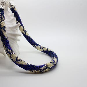 May include: A blue and white beaded necklace with a silver clasp. The necklace is made of small beads and has a geometric pattern.