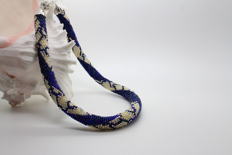 May include: A blue and white beaded necklace with a silver clasp. The necklace is made of small beads and has a geometric pattern.