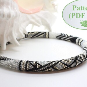 Könnte beinhalten: Eine schwarz-weiße Perlenkette mit geometrischem Muster. Die Kette liegt auf einer weißen Oberfläche neben einer Muschel. Der Text "Pattern (PDF file)" ist im Bild sichtbar.