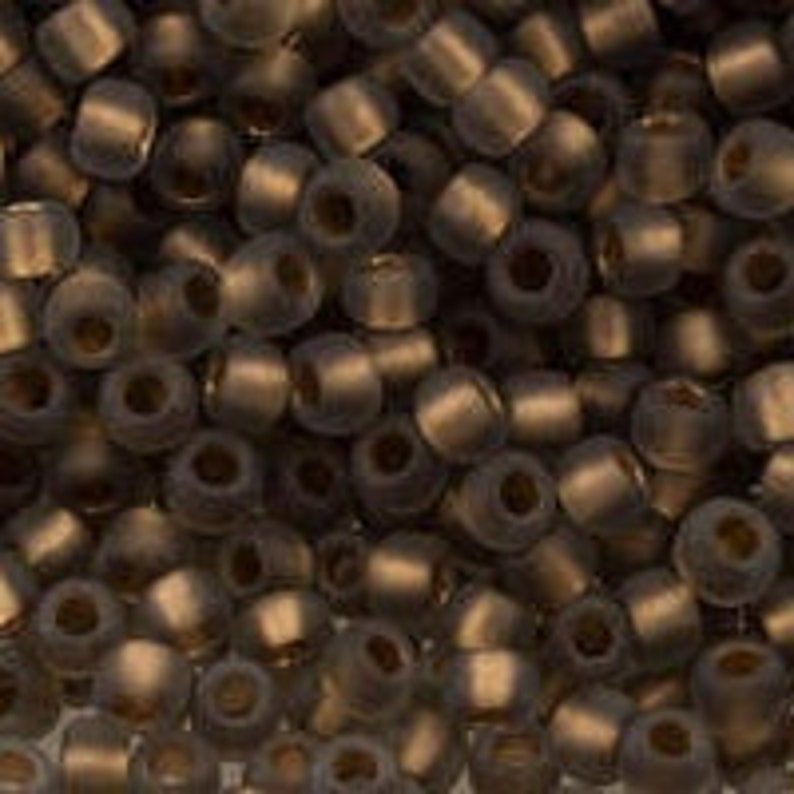 May include: A close-up of a pile of small, dark brown glass seed beads. The beads have a matte finish and are slightly iridescent.