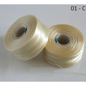 Pode incluir: Dois carret&eacute;is de fio de cor creme. O fio &eacute; enrolado em torno de um carretel de pl&aacute;stico branco com um centro azul.