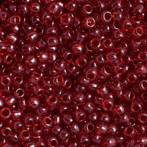 May include: A close-up image of a large quantity of small, round, red glass beads. The beads are translucent and have a slight shine.
