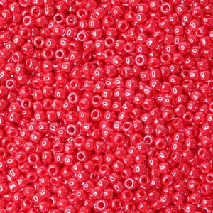 May include: A close-up shot of a mass of small, bright red glass seed beads. Each bead is a tiny cylinder with a central hole, ideal for threading. The beads are densely packed, forming a textured, vibrant surface.