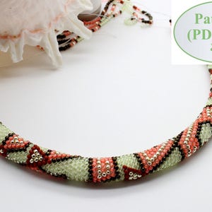 May include: A beaded necklace with a green, brown, and pink geometric pattern. The necklace is coiled and laid on a white surface. The text "Pattern (PDF file)" is visible in the image.