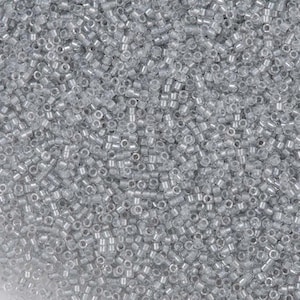 May include: A close-up shot of a large pile of small, cylindrical, silver-colored glass beads. The beads are densely packed together, creating a textured surface. The beads are uniform in size and shape, with a small hole running through the center of each.