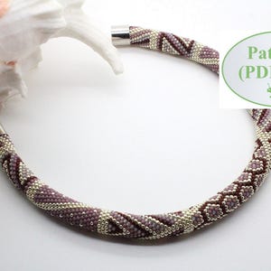 Puede incluir: Un collar de cuentas con un patrón geométrico en tonos de morado y plateado. El collar está hecho con cuentas pequeñas y tiene un cierre plateado. El patrón es un diseño repetitivo de triángulos y cuadrados.