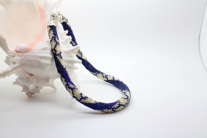 May include: A blue and white beaded necklace with a silver clasp. The necklace is made of small beads and has a snake-like pattern.