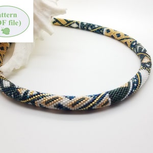 Puede incluir: Un collar de cuentas con un patrón geométrico en tonos de blanco, dorado y verde. El collar está hecho con pequeñas cuentas de semillas y tiene una forma redonda.