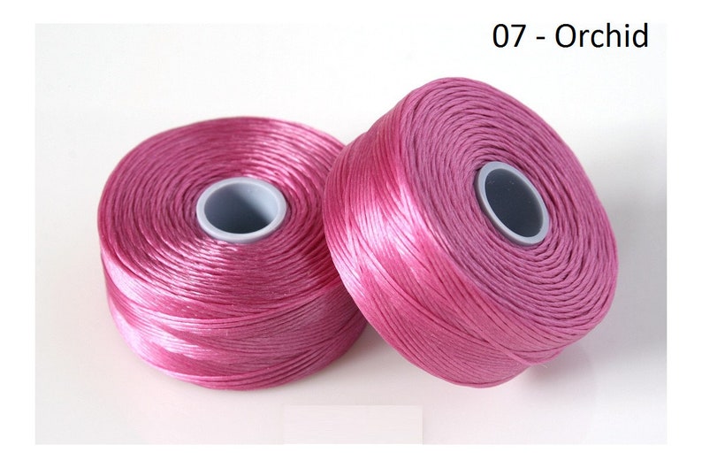 Pode incluir: Dois carret&eacute;is de fio de bordar rosa, etiquetados como "07 - Orchid".