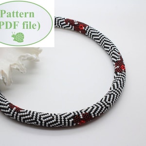May include: A black and white beaded necklace with a geometric pattern and red accents. The necklace is lying on a white surface.