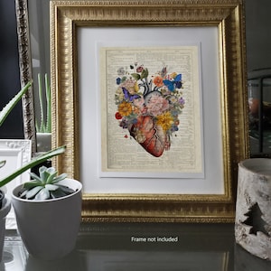 May include: A vintage anatomical heart illustration with colorful flowers and butterflies, printed on a vintage dictionary page. The heart is surrounded by flowers in shades of pink, yellow, and blue. The butterflies are blue and purple. The image is framed in a gold frame.