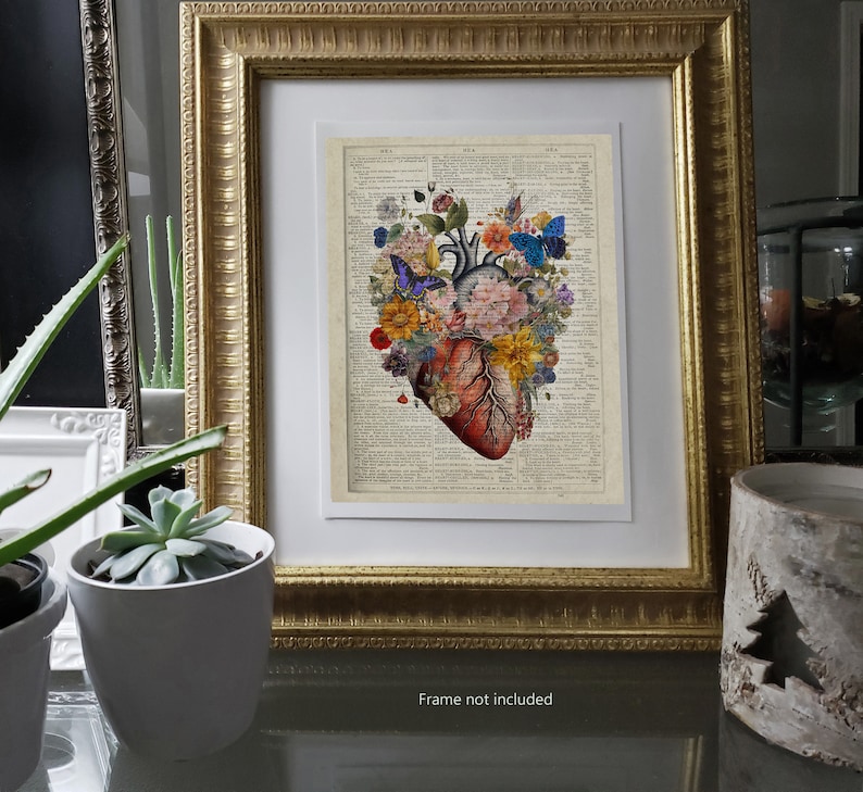 May include: A vintage anatomical heart illustration with colorful flowers and butterflies, printed on a vintage dictionary page. The heart is surrounded by flowers in shades of pink, yellow, and blue. The butterflies are blue and purple. The image is framed in a gold frame.