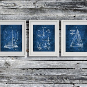 May include: Three white framed prints of vintage sailboat patent drawings on a blue background. The drawings are in black and white and show different views of the sailboat.