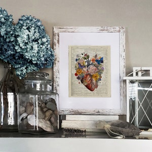 May include: A vintage style print of a human heart with flowers and butterflies. The print is framed in a white distressed frame and is sitting on a shelf with other decorative items.