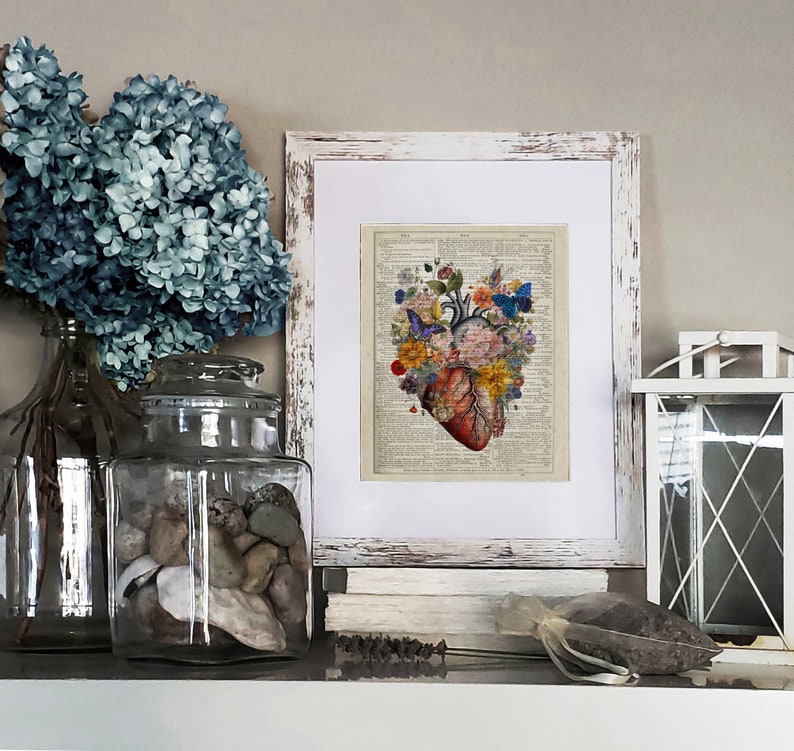 May include: A vintage style print of a human heart with flowers and butterflies. The print is framed in a white distressed frame and is sitting on a shelf with other decorative items.