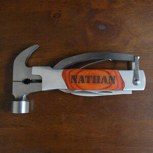 May include: A multi-tool with a hammer head, pliers, and a knife. The handle is made of wood and has the name "NATHAN" engraved on it.