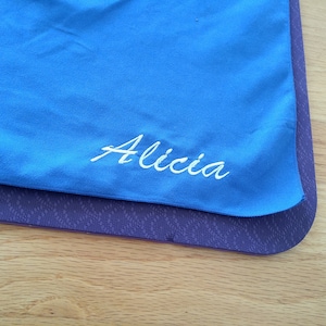 Peut inclure: Une serviette en microfibre bleue avec le nom "Alicia" brodé en blanc.