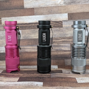 May include: Three small flashlights with different coloured bodies and the words "LIVE", "LAUGH", and "LOVE" engraved on them.
