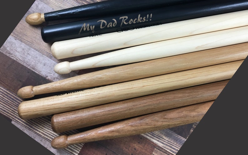 May include: A set of six wooden drumsticks, some with a natural finish and some painted black. One drumstick is engraved with the text "My Dad Rocks!!".