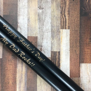 May include: A pair of black wooden drumsticks with the text "Happy Father's Day! My Dad Rocks!!" engraved in gold.