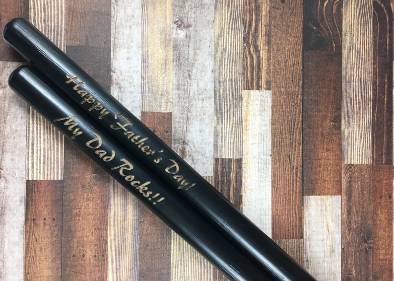 May include: A pair of black wooden drumsticks with the text "Happy Father's Day! My Dad Rocks!!" engraved in gold.