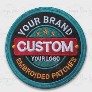 May include: A circular embroidered patch with a black background and a teal border. It features the white text YOUR BRAND, CUSTOM, and YOUR LOGO, with the orange text EMBROIDERED PATCHES. Three small orange stars are centred above the word CUSTOM.