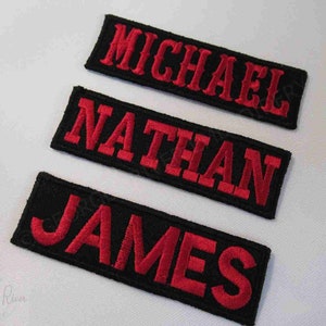 May include: Three black fabric patches with red embroidered lettering. The patches read "MICHAEL", "NATHAN", and "JAMES".