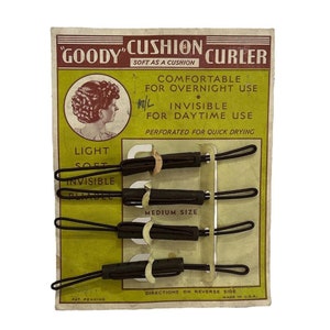 Könnte beinhalten: Eine Vintage-Packung "Goody" Cushion Curlers mit einer Frau mit einer Frisur auf der Vorderseite. Die Packung enthält sechs schwarze Lockenwickler, beschriftet mit "Light", "Soft", "Invisible" und "Medium Size". Die Packung ist gelb mit roten und braunen Akzenten. Der Text "Goody Cushion Curler" ist in Rot und Braun gedruckt. Der Text "Soft as a Cushion" ist in Braun gedruckt. Der Text "Comfortable for Overnight Use" ist in Rot gedruckt. Der Text "Invisible for Daytime Use" ist in Rot gedruckt. Der Text "Perforated for Quick Drying" ist in Braun gedruckt. Der Text "Directions on Reverse Side" ist in Braun gedruckt. Der Text "Made in U.S.A." ist in Braun gedruckt. Der Text "Pat Pending" ist in Braun gedruckt.