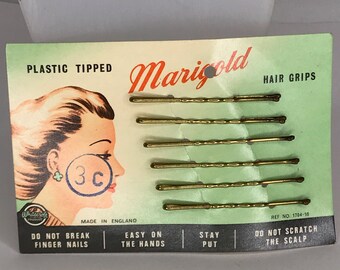 Könnte beinhalten: Eine Vintage-Packung Marigold Haarklammern mit Kunststoffspitzen. Die Packung zeigt eine Frau mit einer Frisur und einem Preisschild von 3c. Die Packung lautet "Nicht an den Fingernägeln brechen, leicht in der Handhabung, hält fest, nicht auf der Kopfhaut kratzen".