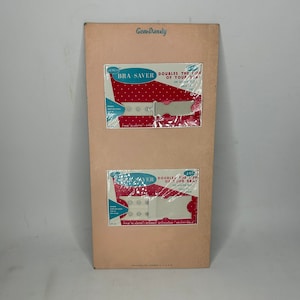 May include: A pink and white cardboard display card with two packages of white plastic bra savers. The packages are labeled "GENCO BRA SAVER" and "DOUBLES THE LIFE OF YOUR BRA!" The packages are both 15 cents.
