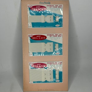 May include: Three white bra strap extenders with metal hooks and eyes. The extenders are packaged on a pink card with blue and white text that reads "Gem-Dandy", "new BRA-LAST", "DOUBLES THE LIFE OF YOUR BRA!" and "FULL 5' LENGTH - ADJUSTABLE".