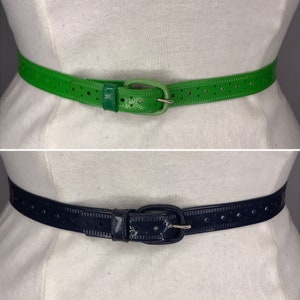 May include: Two belts with a perforated design. The top belt is green and the bottom belt is navy blue.