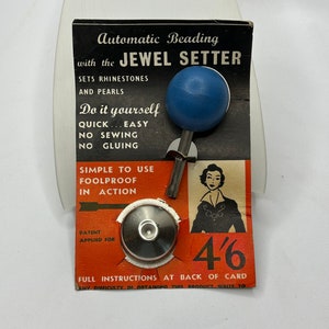 May include: A black and red card with the text "Automatic Beading with the JEWEL SETTER" and "Do it yourself QUICK...EASY NO SEWING NO GLUING" and "SIMPLE TO USE FOOLPROOF IN ACTION". The card also has a blue plastic knob with a metal rod attached to it. The card also has a silver metal setting tool and the text "4'6" and "FULL INSTRUCTIONS AT BACK OF CARD".