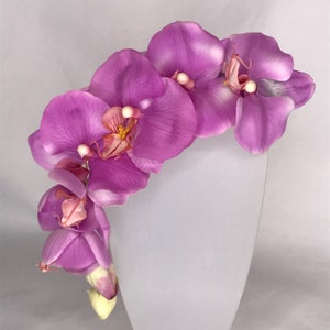May include: A cluster of pink orchid flowers arranged in a curved shape. The flowers are a light pink colour with a darker pink centre and yellow accents.