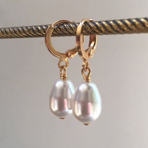 May include: A pair of gold hoop earrings with a single white pearl dangling from each hoop.