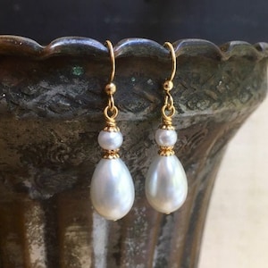 May include: A pair of gold drop earrings with white pear-shaped pearls. The earrings have a simple design and are perfect for everyday wear.