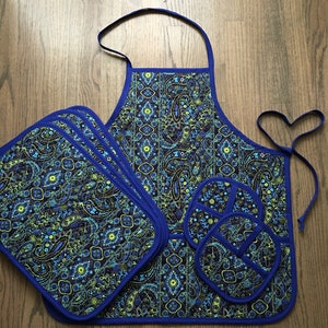 May include: A blue paisley patterned kitchen apron with matching pot holders. The apron has a blue trim and ties around the waist. The pot holders are circular and have a blue trim.
