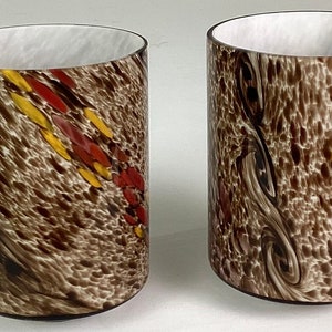 May include: Two clear glass tumblers with a brown, white, red, and yellow speckled pattern. The pattern on the left tumbler is a diagonal stripe, while the pattern on the right tumbler is a swirling pattern.
