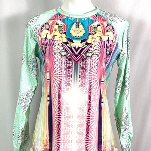 Op de afbeelding: Een shirt met lange mouwen met een kleurrijke, abstracte print met bloemen en geometrische patronen. Het shirt heeft een lichtgroene basiskleur met een wit en zilveren patroon op de mouwen.