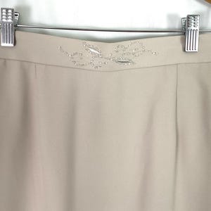 May include: A beige skirt with a beaded floral design at the waistband.aa