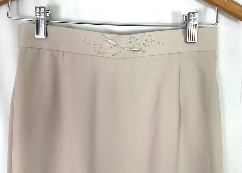 May include: A beige skirt with a beaded floral design at the waistband.aa