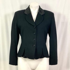 May include: A black blazer with a decorative collar and button closure. The blazer has a scalloped hemline and long sleeves. The collar is embellished with a textured design.