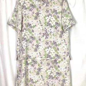 May include: A light pink dress with a floral print featuring white, purple, and green flowers. The dress has a round neckline and short sleeves. The dress is made by Pendleton.