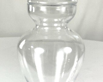 May include: A clear glass jar with a decorative lid. The jar has a wide base and a narrow neck. The lid has a knob on top.