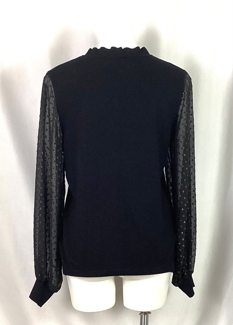K&ouml;nnte beinhalten: Schwarzer Langarm-Pullover mit durchsichtigen &Auml;rmeln mit wei&szlig;en Punkten. Die &Auml;rmel sind am Handgelenk gerafft.