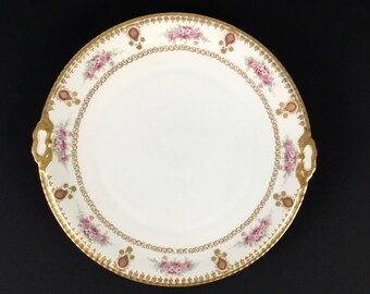 May include: A white porcelain serving platter with a gold rim and floral design. The platter has two handles on the sides.