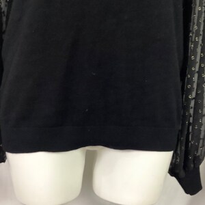 K&ouml;nnte beinhalten: Schwarzer Pullover mit langen &Auml;rmeln und einem schwarzen und goldenen T&uuml;ll&uuml;berzug mit Punkten an den &Auml;rmeln.
