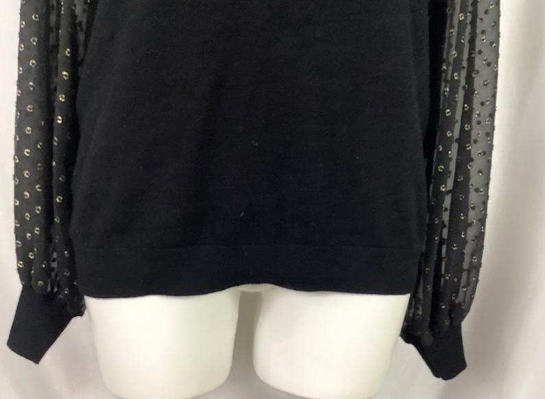 K&ouml;nnte beinhalten: Schwarzer Pullover mit langen &Auml;rmeln und einem schwarzen und goldenen T&uuml;ll&uuml;berzug mit Punkten an den &Auml;rmeln.